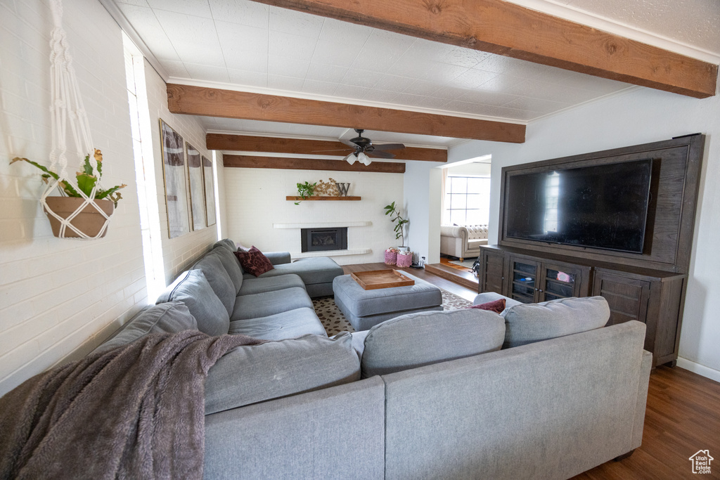 Living area featuring dark wood finished floors, a ceiling fan, beam ceiling, and a fireplace with raised hearth