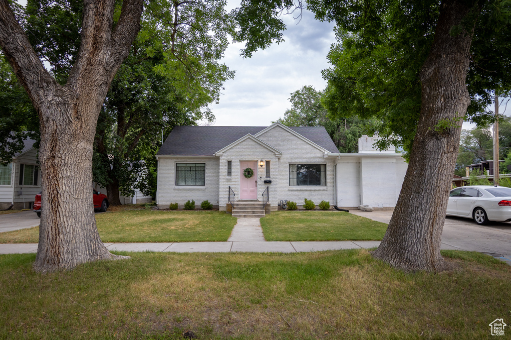 View of front of property featuring brick siding, a front yard, concrete driveway, and a chimney