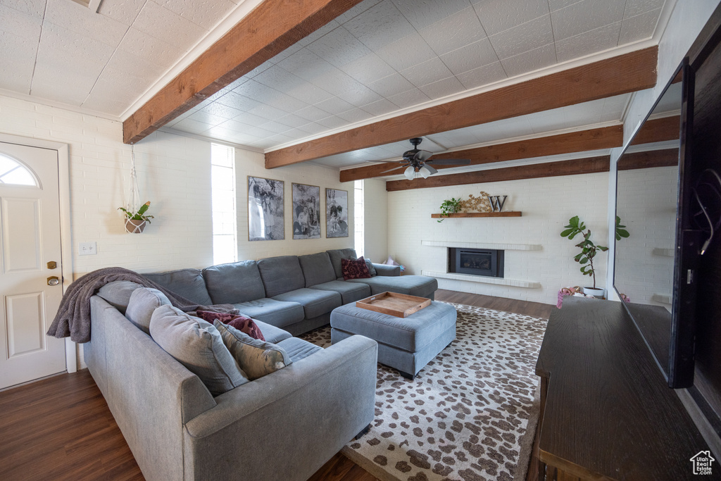 Living area featuring dark wood-style flooring, beamed ceiling, a ceiling fan, and a fireplace with raised hearth