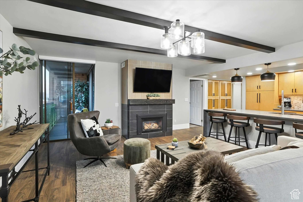 Living area with beam ceiling, dark wood finished floors, a tiled fireplace, a chandelier, and recessed lighting