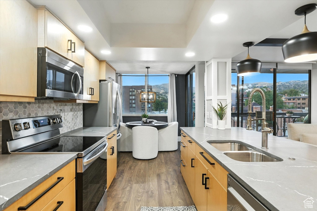 Kitchen featuring stainless steel appliances, dark wood-type flooring, tasteful backsplash, hanging light fixtures, and light brown cabinets