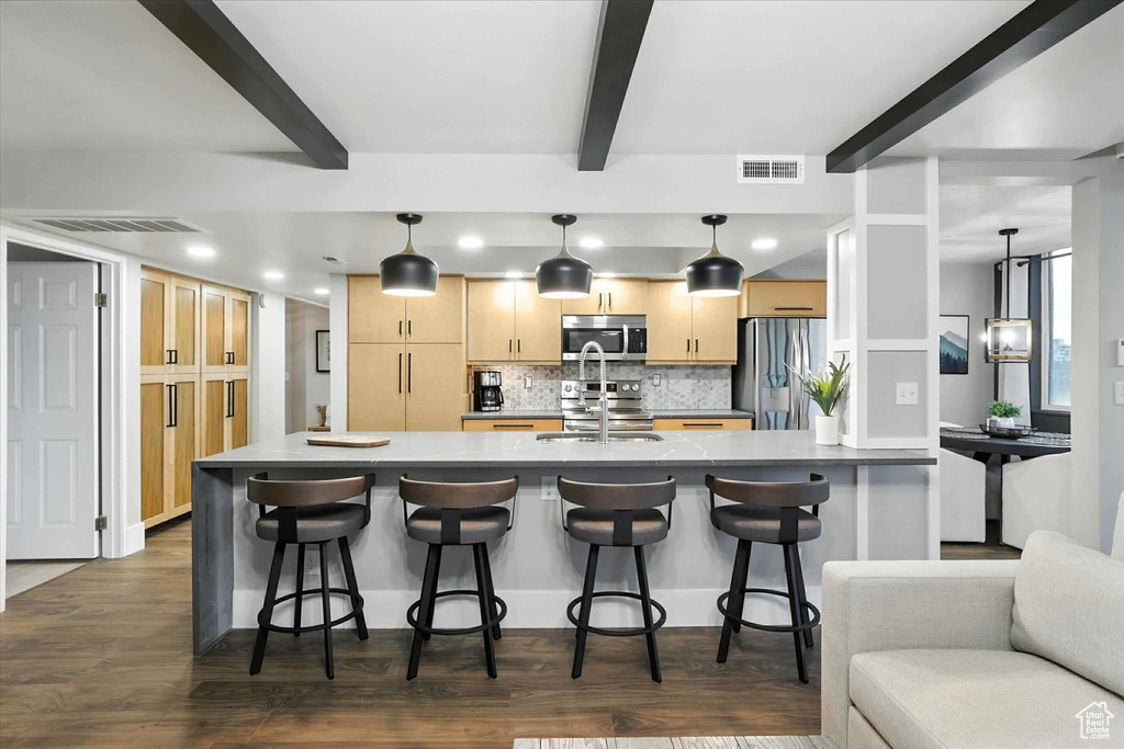 Kitchen with light brown cabinets, decorative backsplash, stainless steel appliances, dark wood-style floors, and beamed ceiling