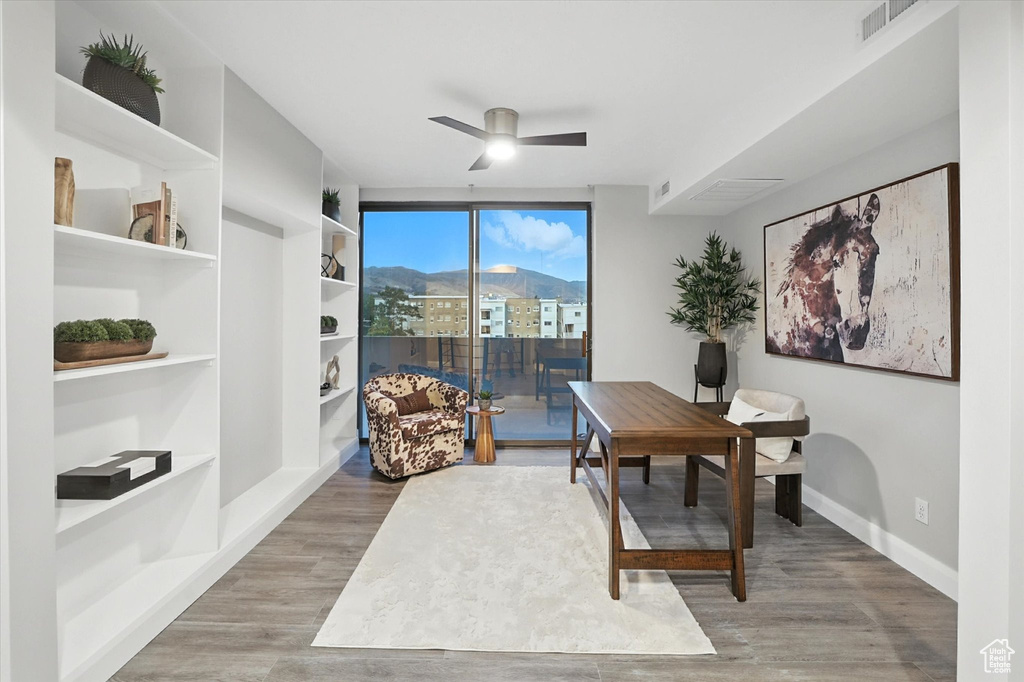 Home office with a ceiling fan, light wood-style floors, built in shelves, and a mountain view