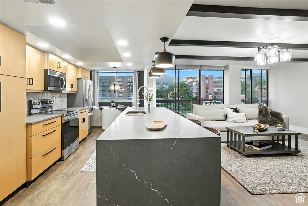 Kitchen featuring light brown cabinetry, stainless steel appliances, light wood-type flooring, a center island with sink, and a chandelier
