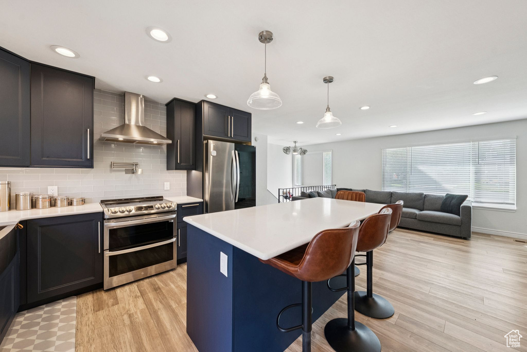 Kitchen with stainless steel appliances, wall chimney exhaust hood, light countertops, a kitchen breakfast bar, and recessed lighting