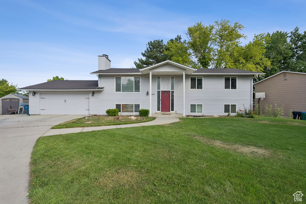 Bi-level home featuring driveway, an attached garage, a chimney, and a front lawn