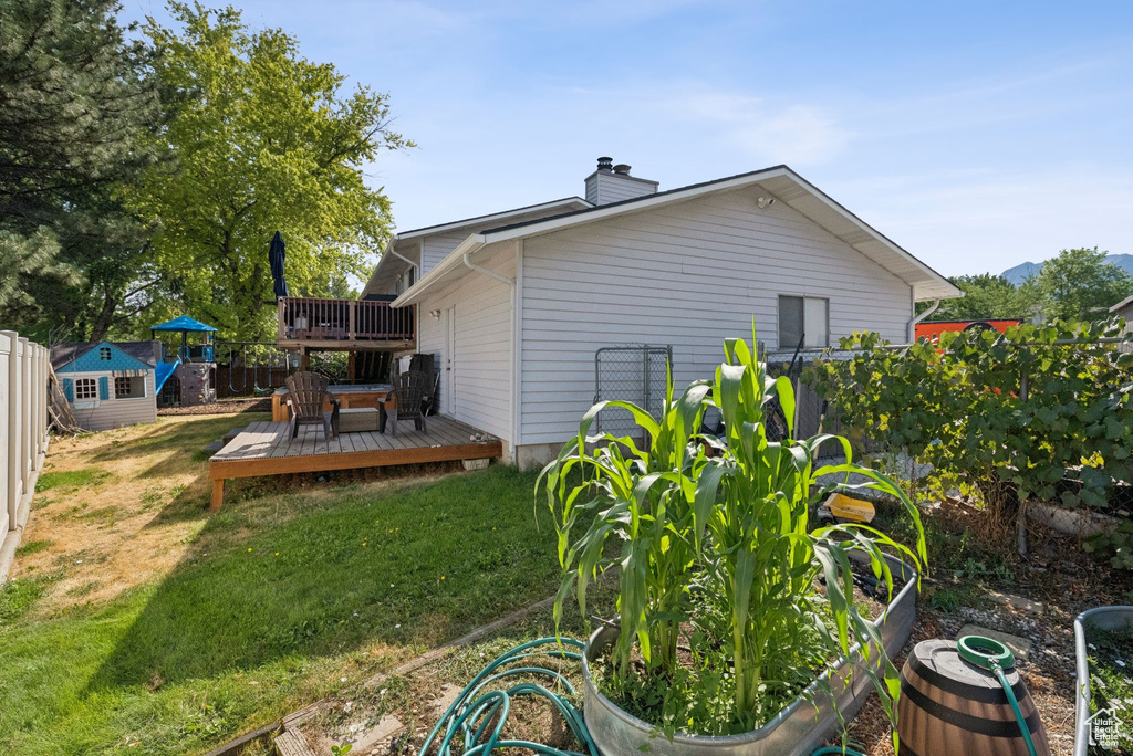 Back of property featuring a wooden deck, a lawn, a chimney, and a storage unit