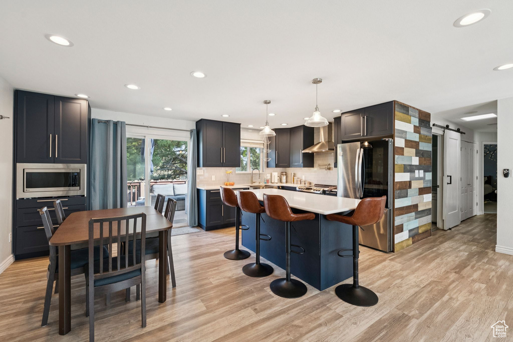Kitchen with a barn door, stainless steel appliances, light countertops, a kitchen breakfast bar, and tasteful backsplash