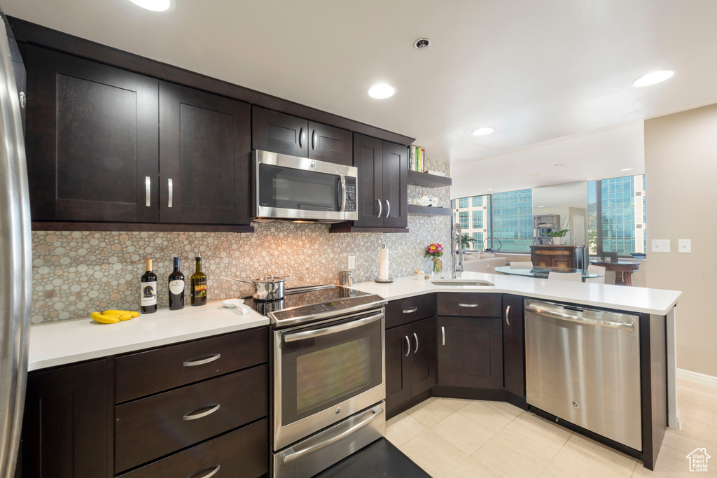 Kitchen featuring appliances with stainless steel finishes, a peninsula, backsplash, light countertops, and dark brown cabinets