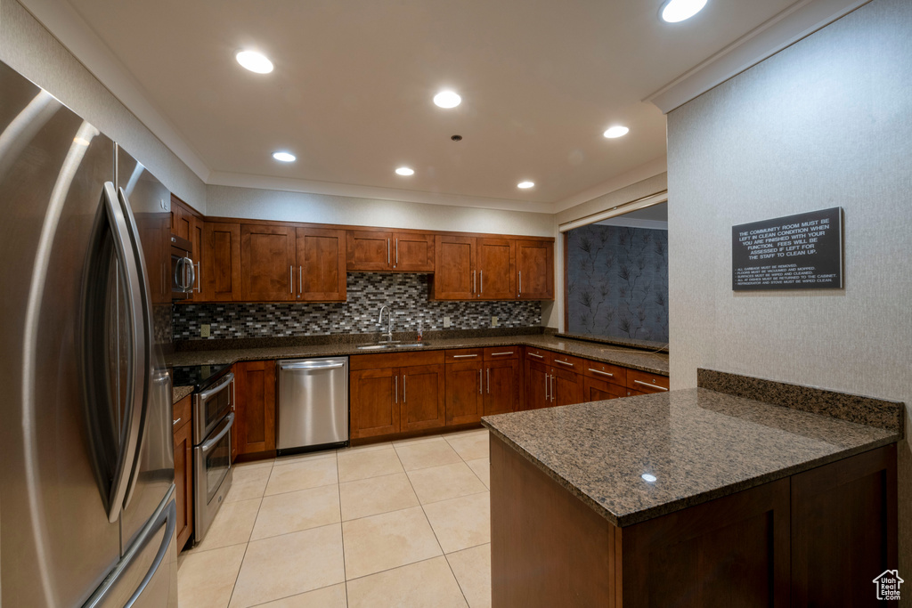 Kitchen featuring stainless steel appliances, decorative backsplash, light tile patterned flooring, dark stone countertops, and a peninsula