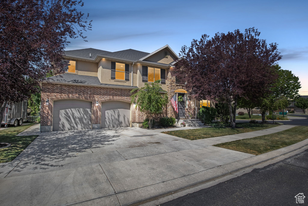 View of front of home with an attached garage, stucco siding, driveway, brick siding, and a shingled roof