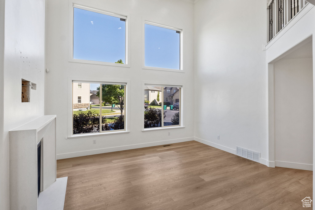 Unfurnished living room with a high ceiling, light wood-type flooring, plenty of natural light, and a fireplace