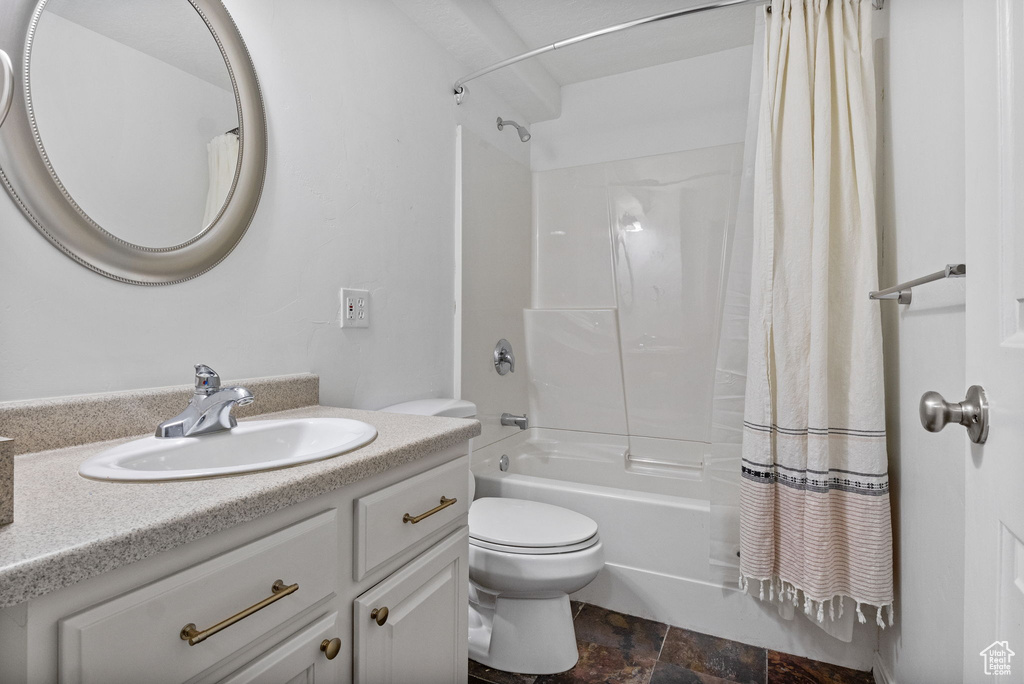 Bathroom featuring vanity, shower / bathtub combination with curtain, and stone finish flooring