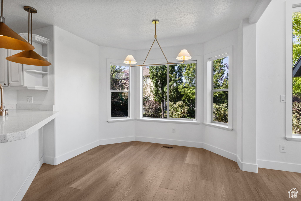 Unfurnished dining area with light wood-style flooring and a textured ceiling