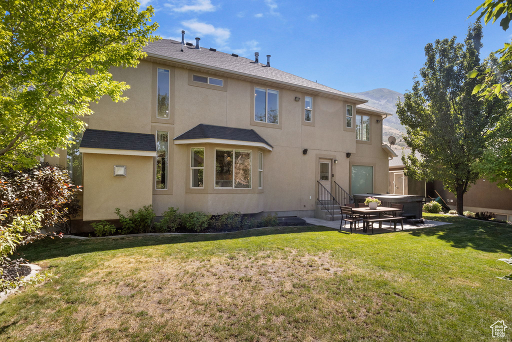 Back of property featuring entry steps, a patio, a lawn, stucco siding, and a mountain view