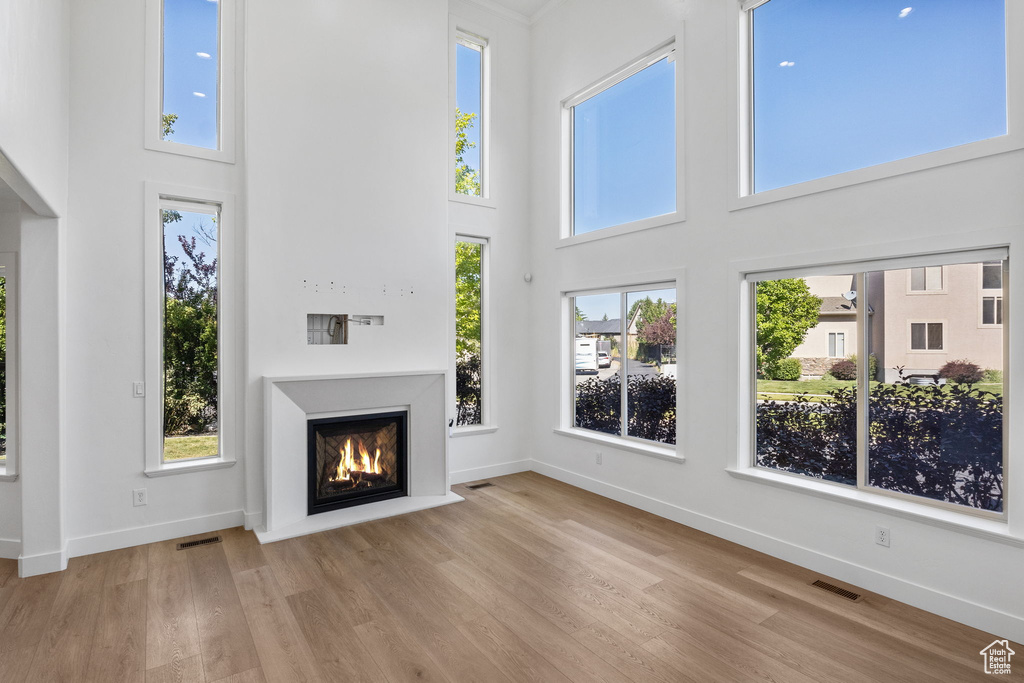 Unfurnished living room with a high ceiling, a warm lit fireplace, wood finished floors, and healthy amount of natural light