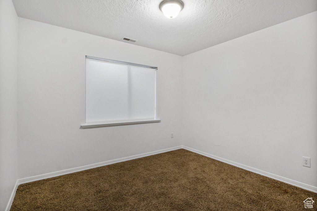 Unfurnished room featuring dark colored carpet and a textured ceiling