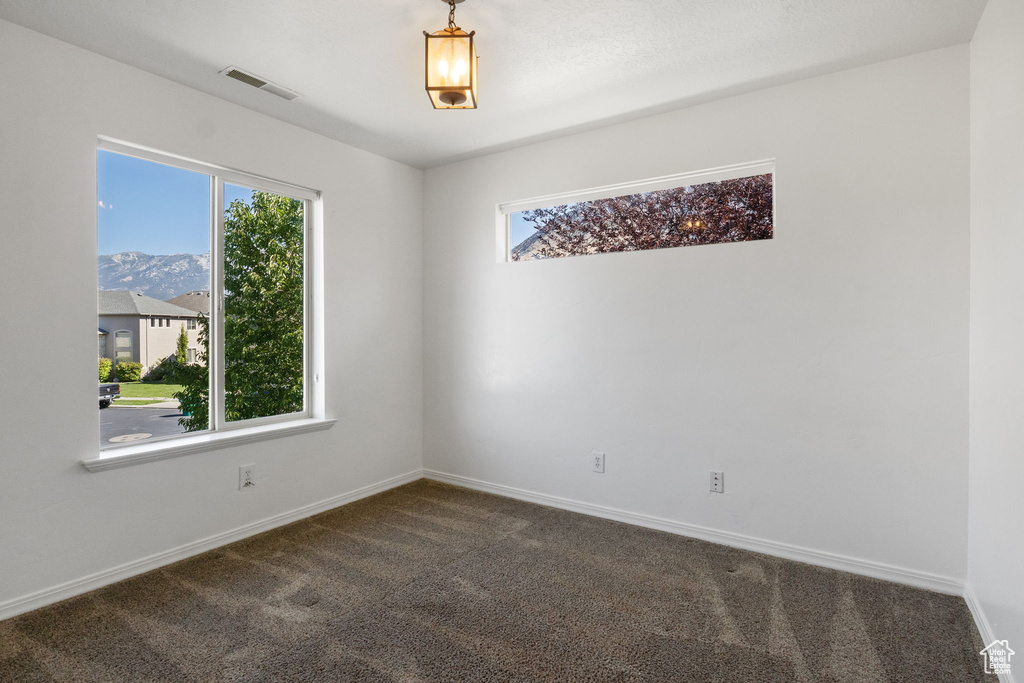 Empty room featuring healthy amount of natural light, dark colored carpet, and a mountain view
