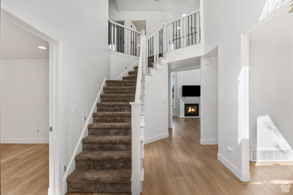Stairs featuring wood finished floors, a towering ceiling, ornamental molding, a lit fireplace, and recessed lighting