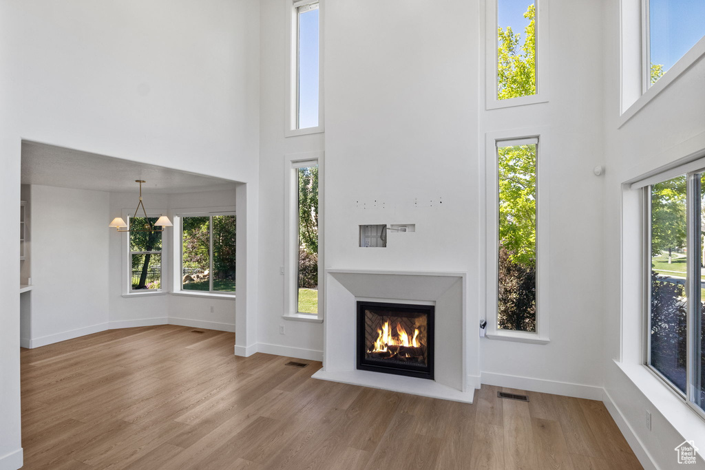 Unfurnished living room with a high ceiling, a chandelier, a warm lit fireplace, and wood finished floors