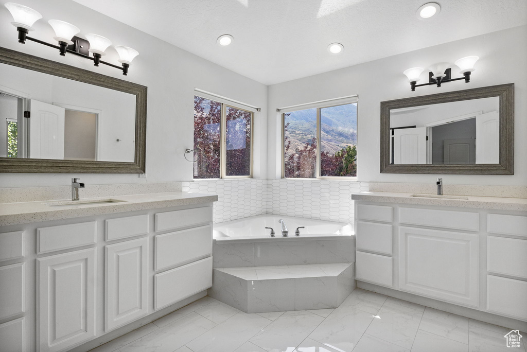 Bathroom featuring marble look tile flooring, two vanities, a garden tub, and recessed lighting