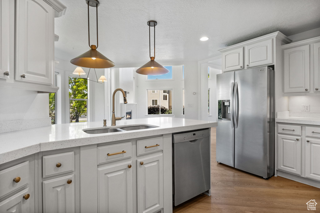 Kitchen with appliances with stainless steel finishes, white cabinets, recessed lighting, decorative light fixtures, and wood finished floors