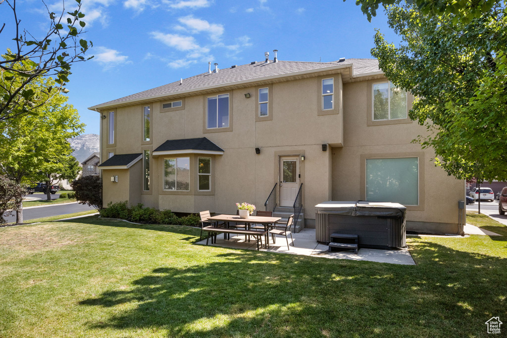 Rear view of house with a hot tub, stucco siding, a patio area, a yard, and a shingled roof