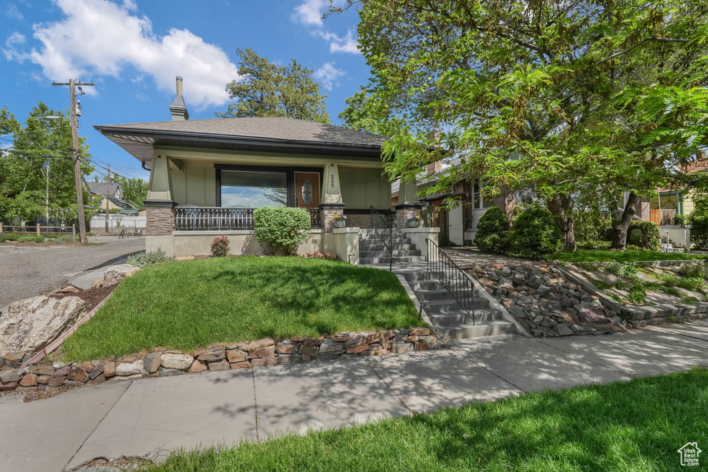 View of front of house featuring a chimney, a porch, a shingled roof, and a front lawn