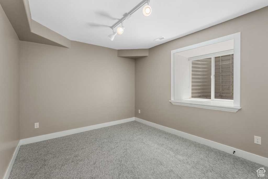 Carpeted empty room featuring baseboards and track lighting