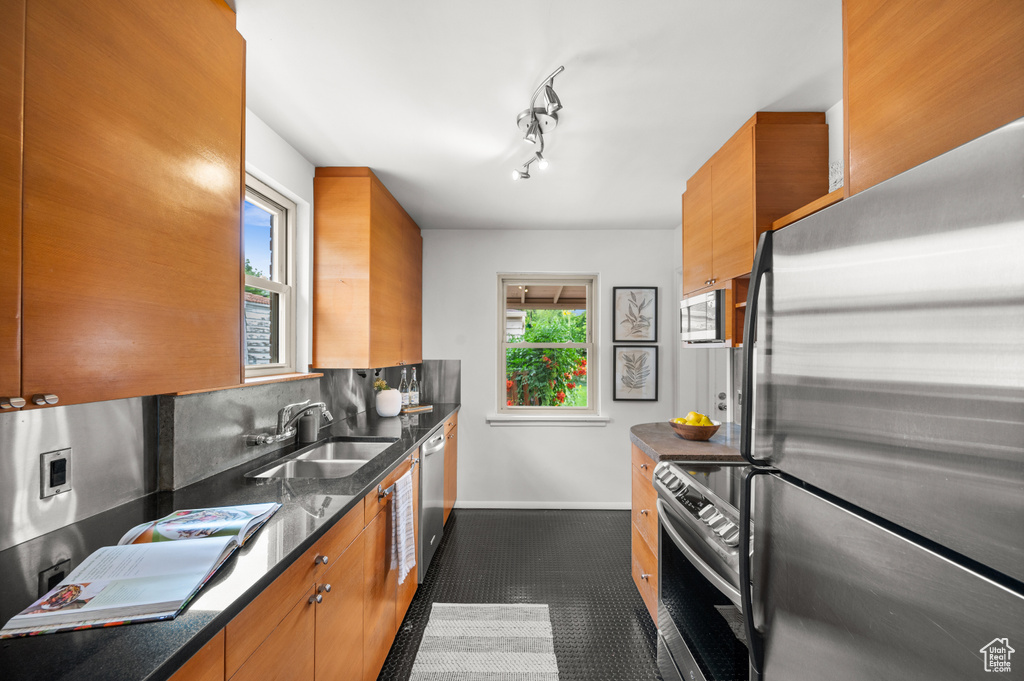Kitchen with stainless steel appliances, brown cabinetry, and dark stone counters