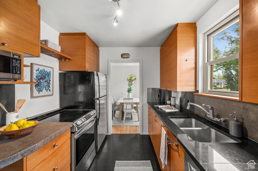 Kitchen featuring stainless steel appliances, dark countertops, open shelves, and brown cabinetry
