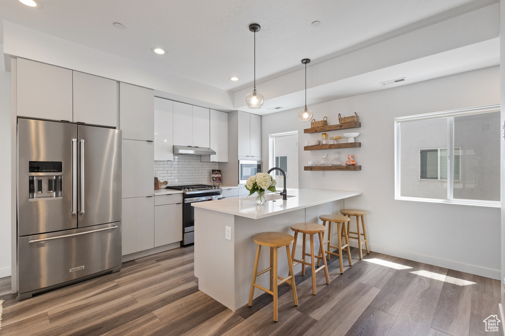 Kitchen featuring appliances with stainless steel finishes, wood finished floors, a kitchen bar, a peninsula, and recessed lighting