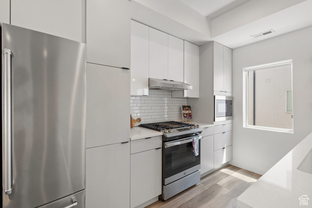 Kitchen featuring stainless steel appliances, light countertops, light wood-type flooring, white cabinetry, and decorative backsplash