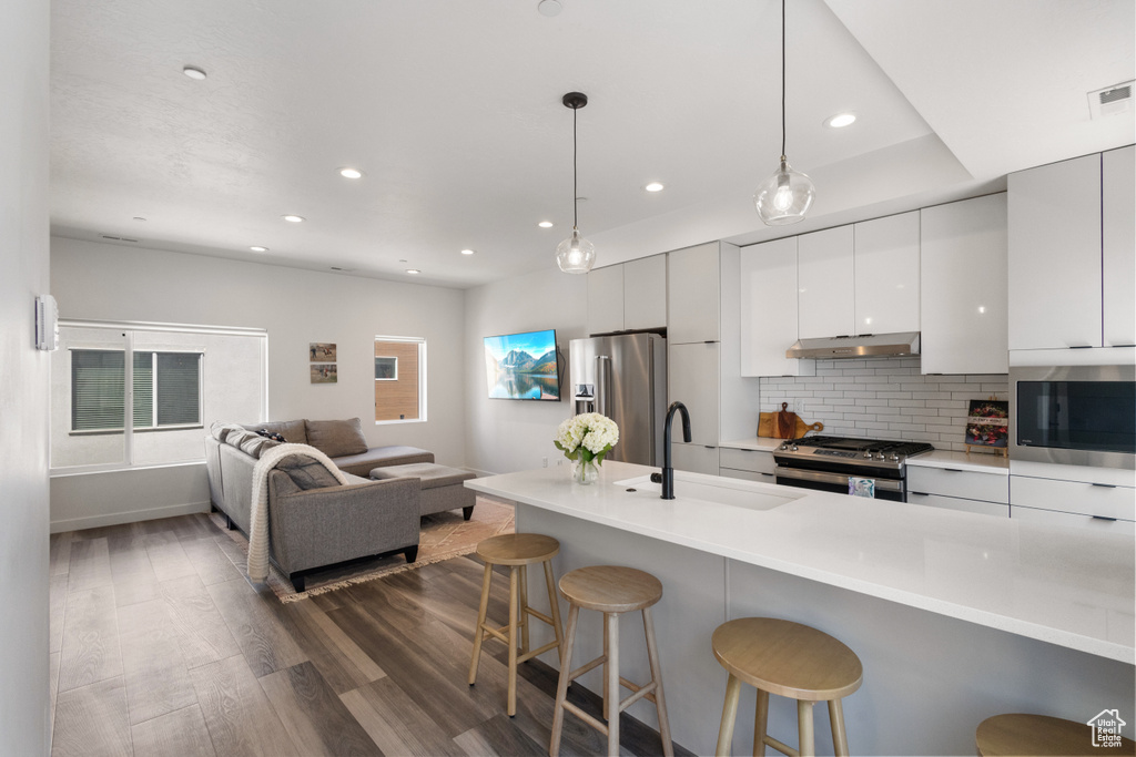 Kitchen featuring modern cabinets, dark wood-style flooring, a kitchen bar, appliances with stainless steel finishes, and recessed lighting