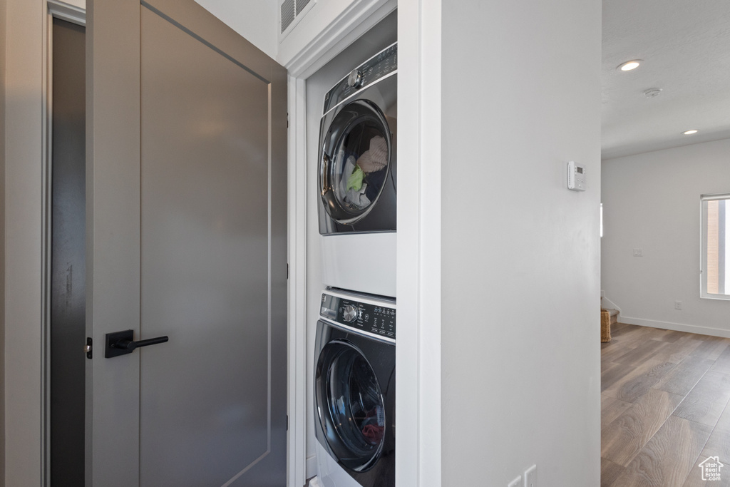 Washroom featuring stacked washer and clothes dryer, wood finished floors, and recessed lighting