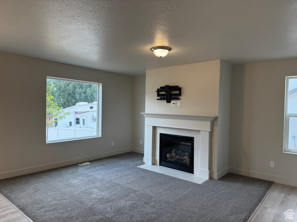 Unfurnished living room with a tiled fireplace, a textured ceiling, and wood finished floors