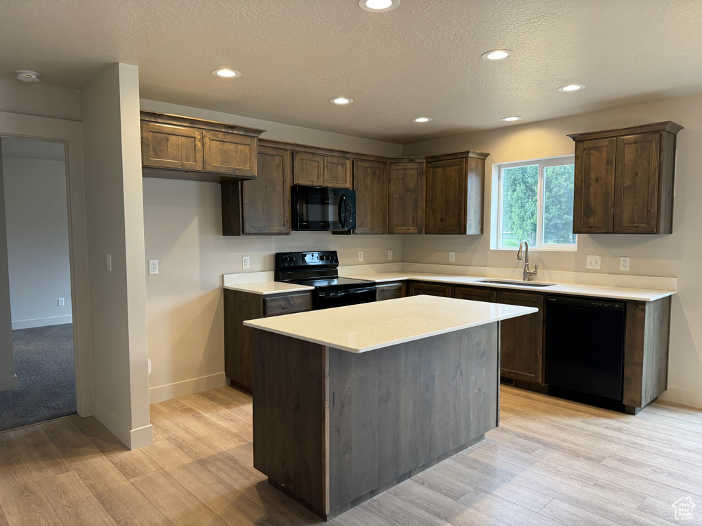 Kitchen featuring black appliances, light wood-style flooring, a center island, recessed lighting, and light countertops