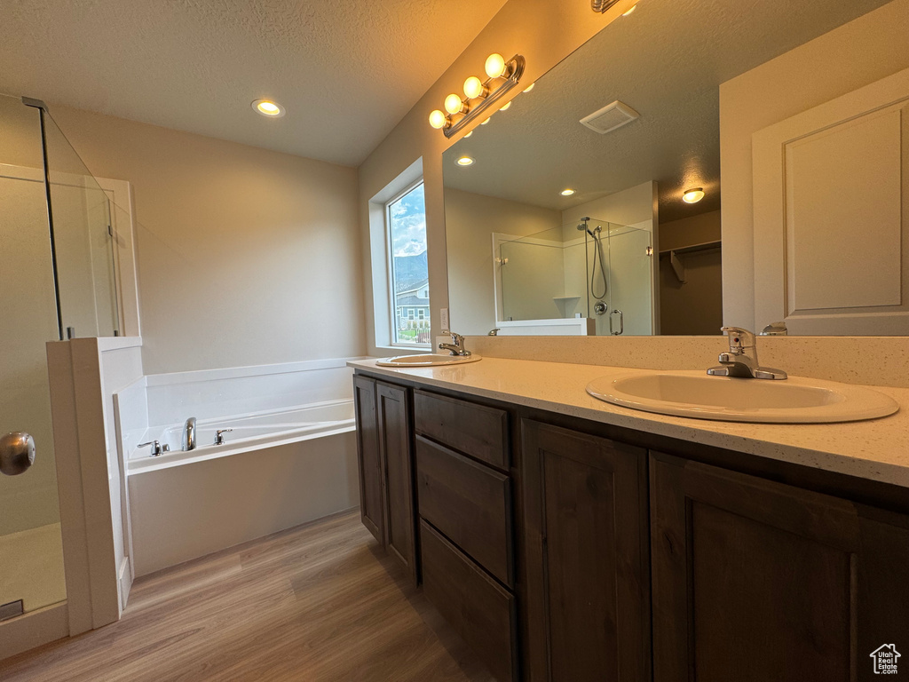 Full bathroom featuring a shower stall, wood finished floors, a garden tub, double vanity, and a textured ceiling