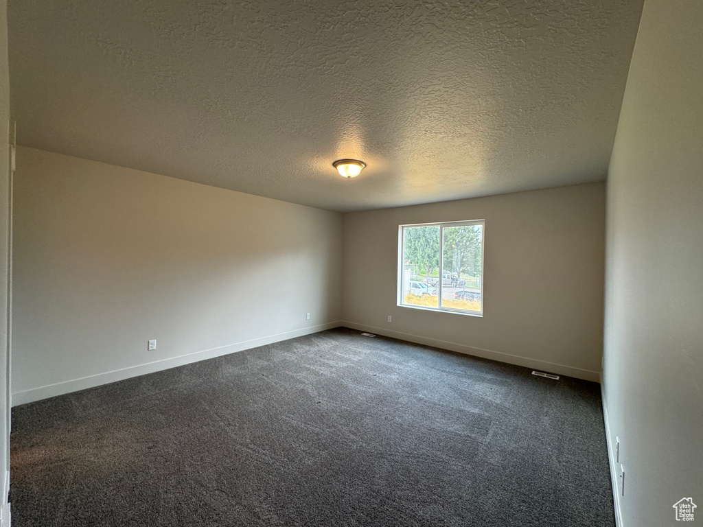 Empty room featuring a textured ceiling and dark colored carpet