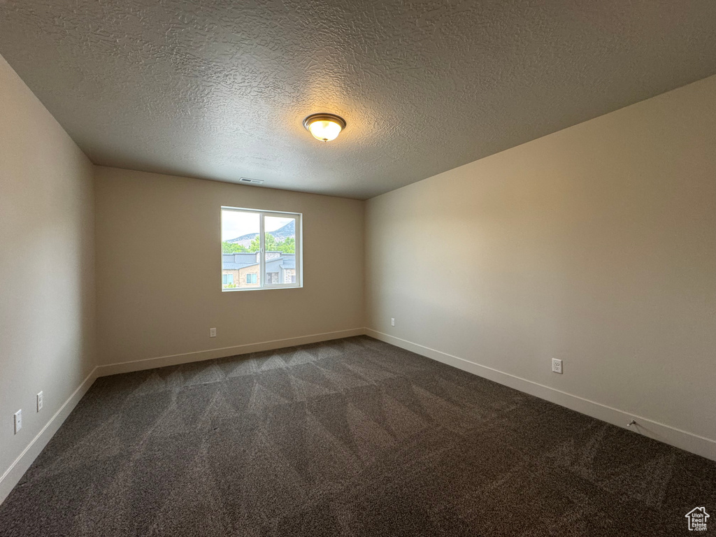 Unfurnished room featuring dark colored carpet and a textured ceiling