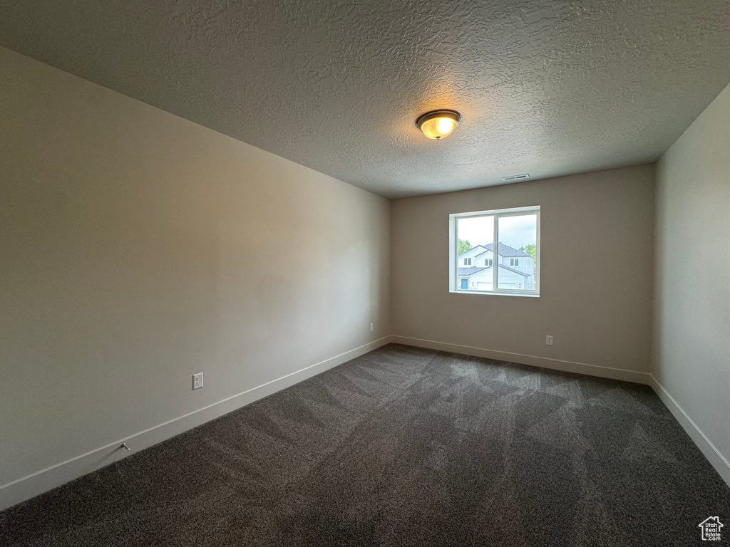 Unfurnished room featuring dark carpet and a textured ceiling