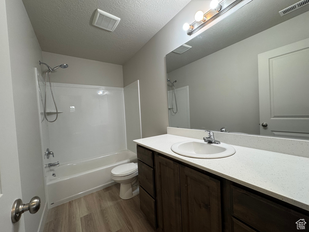 Bathroom featuring wood finished floors, shower / bath combination, vanity, and a textured ceiling