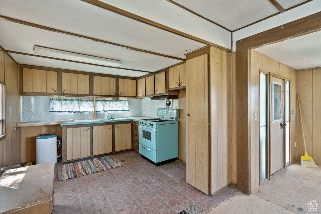 Kitchen with white range with gas cooktop, wood walls, and light countertops