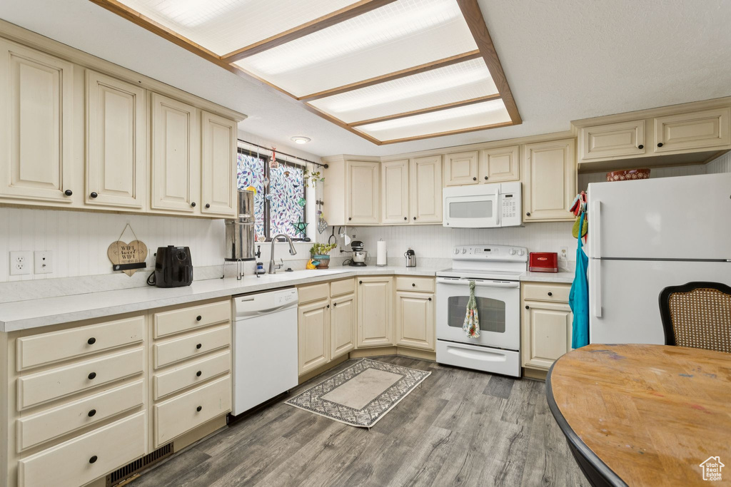 Kitchen with cream cabinets, white appliances, and wood finished floors