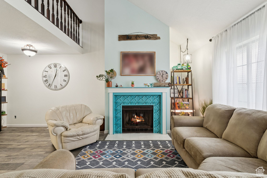 Living area with wood finished floors, a tiled fireplace, and high vaulted ceiling