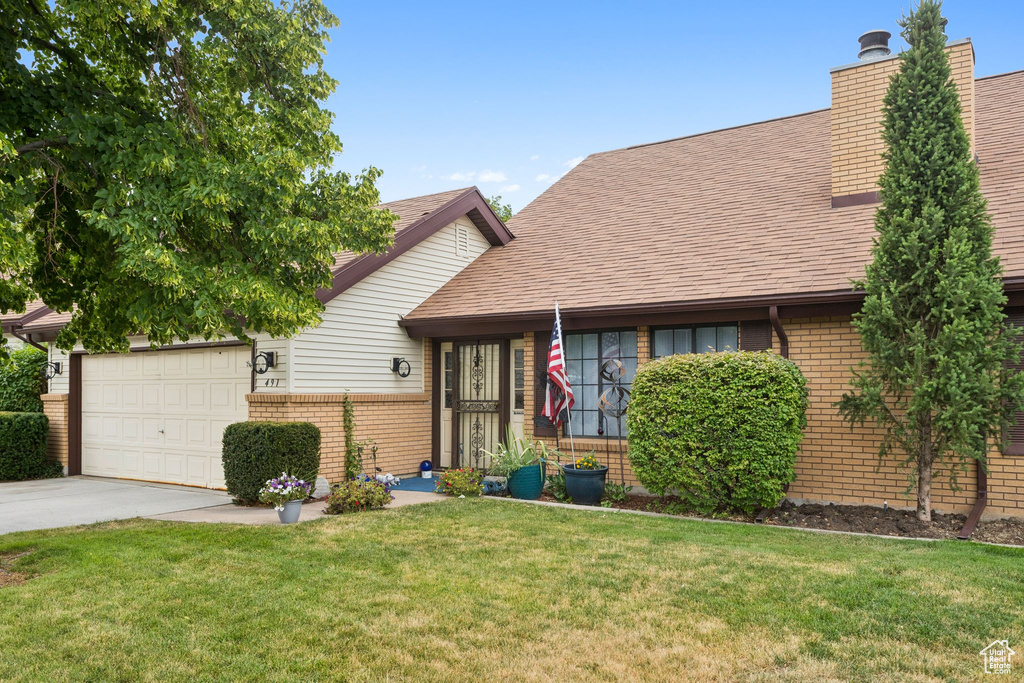 View of front of home featuring brick siding, a garage, a front lawn, driveway, and a chimney