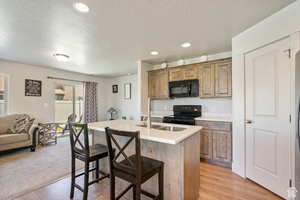 Kitchen with black appliances, a breakfast bar, a textured ceiling, light wood-style floors, and a kitchen island with sink