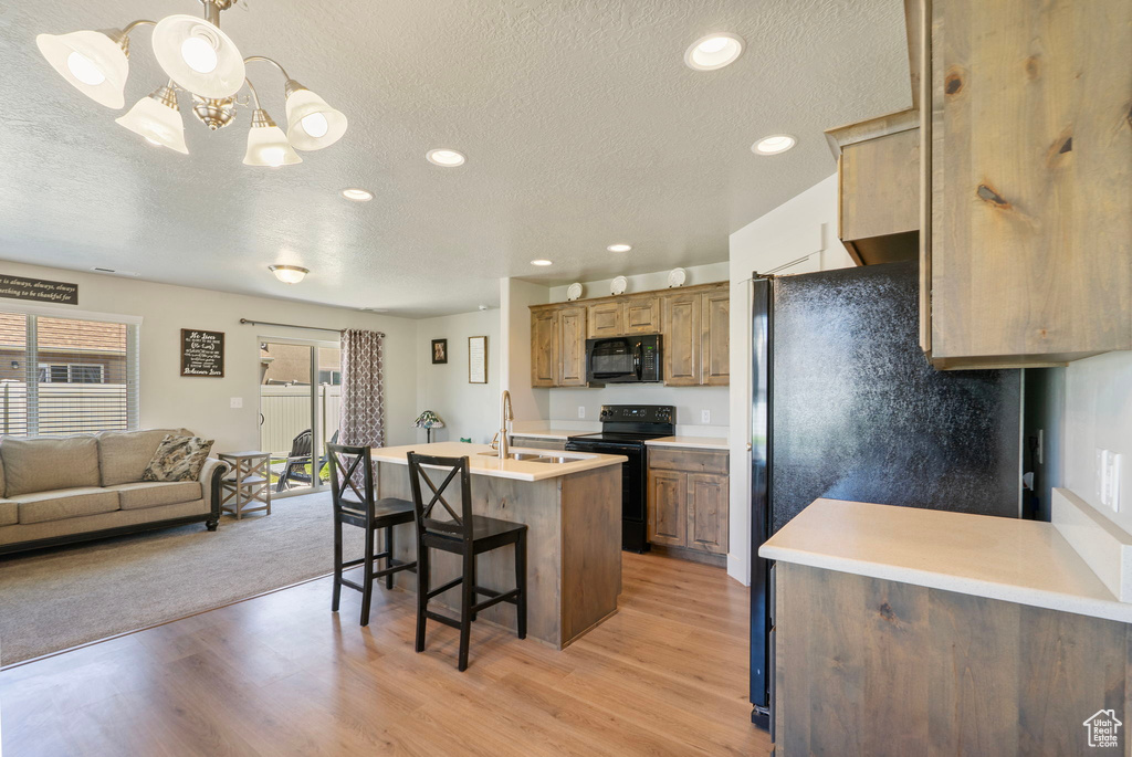 Kitchen with black appliances, a textured ceiling, a breakfast bar, light countertops, and open floor plan