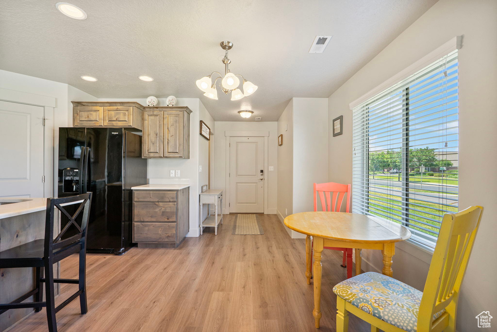 Kitchen with black refrigerator with ice dispenser, a chandelier, light wood-style floors, hanging light fixtures, and recessed lighting