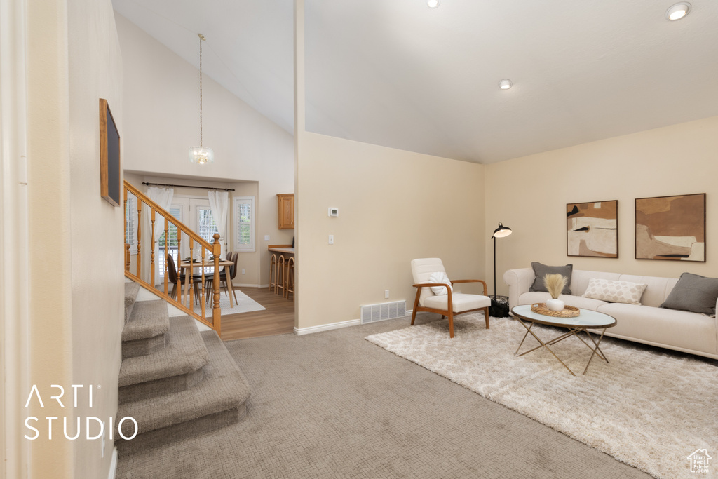 Living area featuring high vaulted ceiling, stairs, light carpet, and a chandelier